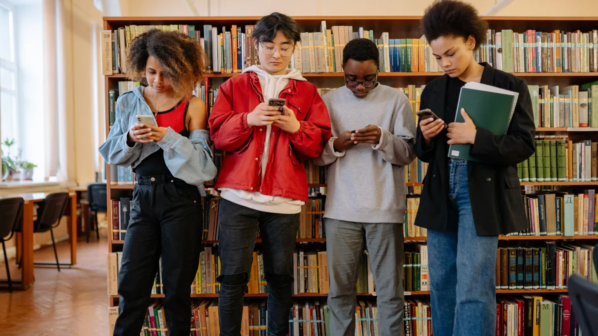 Estudiantes consultan sus teléfonos en una biblioteca, mientras Noruega restringe el uso de inteligencia artificial para menores de 6 a 13 años.