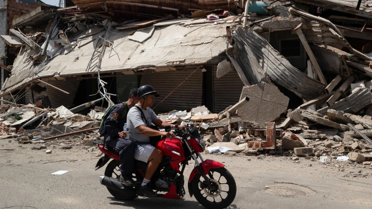 Personas transitan en motocicleta frente a edificios colapsados por los terremotos en Catia La Mar, Venezuela.