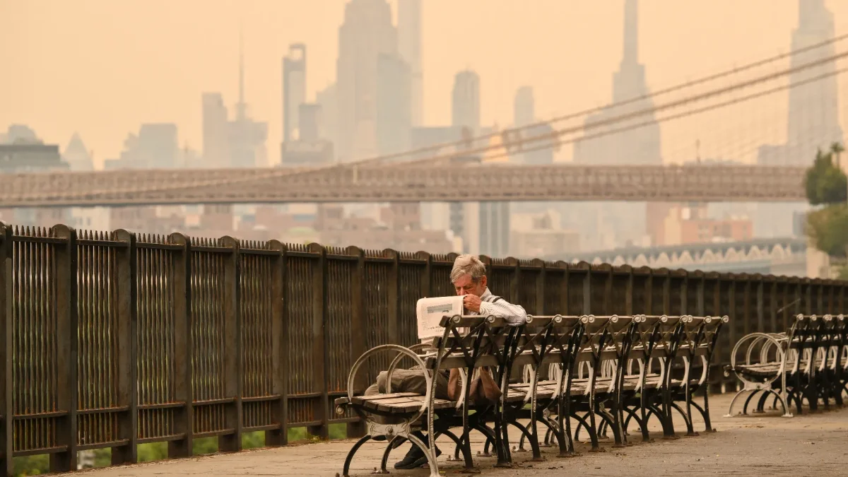 Una persona sentada en un banco lee un periódico mientras el humo de los incendios forestales provenientes de Canadá provoca una densa neblina el 16 de julio de 2026 en Nueva York.