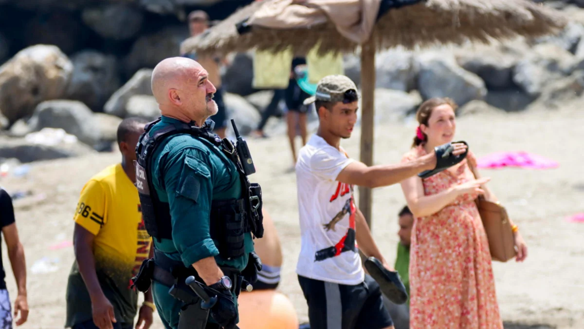 Un agente coordina con vecinos en la playa de Ceuta durante la llegada masiva de migrantes desde Marruecos.