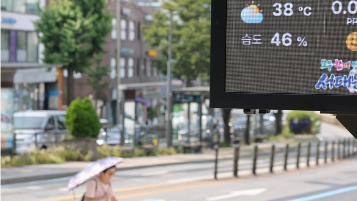 Un tablero digital muestra 38 °C en una calle de Pyongyang, mientras un transeúnte se protege del sol con sombrilla en plena ola de calor.