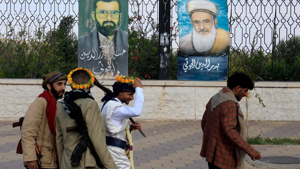 Personas armadas pasan junto a pinturas que representan a líderes hutíes fallecidos, expuestas en una valla en Saná, Yemen, el 7 de septiembre de 2026.
