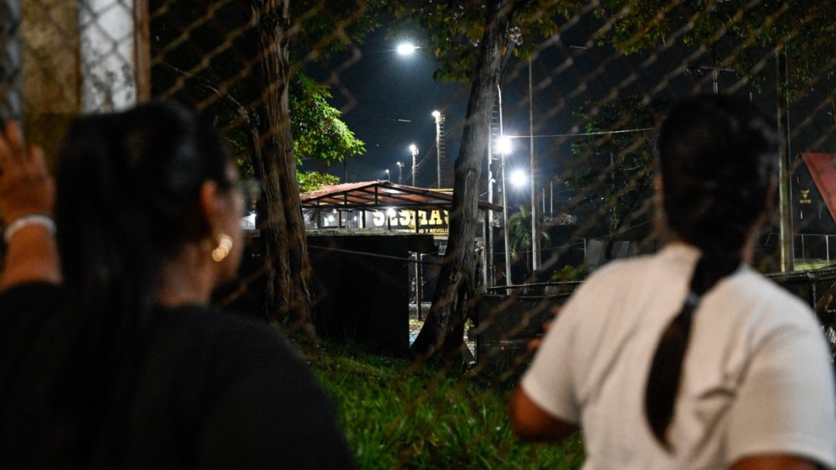 Unas mujeres miran a través de una valla durante una vigilia para exigir la liberación de los presos políticos venezolanos frente a la prisión El Rodeo I en Guatire.