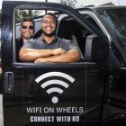 Roman Reyna (L) owner of JFK transportation and Kevin Watson (R), president of JFK transportation, pose with one of their company vans equipped as a mobile Wifi Hotspot to help students access internet to remotely attend their classes, September 16, 2020, in Santa Ana, California. - A minivan with a Wi-fi router attached to the dashboard and a satellite antenna on the roof is helping 200 disadvantaged students in Santa Ana, close to Los Angeles, cope with the rigors of distance learning during the coronavirus pandemic. (Photo by VALERIE MACON / AFP)