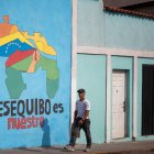 Transeúntes caminando frente a un mural con el mapa de Venezuela que dice "El Esequibo es nuestro", en Caracas.
