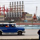 Un auto viejo de transporte colectivo al pasar frente a una planta flotante de generación eléctrica en el puerto de La Habana (Cuba).