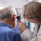 Experienced retired female physician inspecting ear of elderly male patient in clinic office. Closeup of skilled old doctor using otoscope during medical consultation of senior white man.