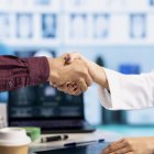Indian general practitioner greeting her male patient at a medical examination, sharing a handshake and discussing about diagnostic reports. Woman doctor helping man to treat an illness. Close up.