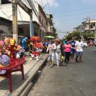 Los visitantes de la calle 6 de marzo caminan por la calzada, cerca de los carros.