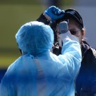 Workers in protective clothes measures the body temperature of a passenger disembarking from the Diamond Princess cruise ship, in quarantine due to fears of new COVID-19 coronavirus, at Daikoku pier cruise terminal in Yokohama on February 21, 2020. - Hundreds of people have been allowed to leave the ship after testing negative for the disease and many have returned to their home countries to face further quarantine. (Photo by Philip FONG / AFP)
