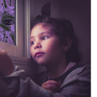 Un niño observa con melancolía desde la ventande su casa.