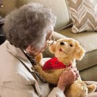 Fotografía cedida por el Departamento para Asuntos de la Tercera Edad de Florida (DOEA) donde se muestra a una anciana mientras disfruta un momento de compañía con un perro robótico de la empresa Joy for All.