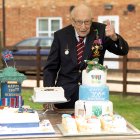 A handout picture released on April 30, 2020 shows Captain Tom Moore posing for a photograph with cakes to celebrate his 100th birthday in Marston Moretaine, north of London. (Photo by Emma SOHL / CAPTURE THE LIGHT / AFP) / RESTRICTED TO EDITORIAL USE - MANDATORY CREDIT "AFP PHOTO / CAPTURE THE LIGHT / EMMA SOHL" - NO MARKETING NO ADVERTISING CAMPAIGNS - DISTRIBUTED AS A SERVICE TO CLIENTS --- NO ARCHIVE ---