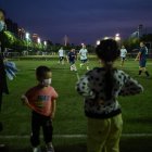 Un grupo de aficionados juegan fútbol en Wuhan, mientras son observados por personas con mascarillas.
