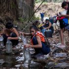 Cientos de ciudadanos recogen agua de un riachuelo.