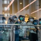 Ciudadanos con mascarilla observan a los manifestantes de una protesta contra la nueva ley de seguridad nacional para Hong Kong tras la cristalera de una tienda, el 1 de julio de 2020 en la ciudad china