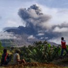 Villagers watch the eruption of Mount Sinabung as seen from Karo, North Sumatra on August 13, 2020. - Indonesia"s Mount Sinabung erupted again on August 13 with a string of blasts that sent plumes of ash two kilometres (1.2 miles) into sky, triggering a flight warning and fears of lava flows. (Photo by ANTO SEMBIRING / AFP)