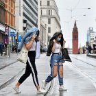 Two women wearing protective face masks cross tram tracks in the rain in Birmingham, central England on August 22, 2020, as Britain"s second-city, home to more than one million people, was made an "area of enhanced support", because of concern about a spike in cases of the novel coronavirus. (Photo by JUSTIN TALLIS / AFP)