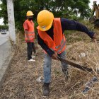 Trabajadores cortan la maleza antes de iniciar la construcción del cerramiento.