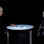Una persona y un robot humanoide participan en un juego competitivo, mientras se mide su actividad cerebral con un electroencefalograma.