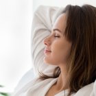 Beautiful 30s woman closed eyes put hands behind head relaxing on comfortable sofa in cozy warm light living room with houseplants, no stress concept, horizontal photo banner for website header design