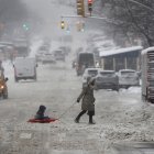 Una mujer y un niño sobre un trineo fueron registrados este sábado al cruzar una calle cubierta de nieve en Nueva York (NY, EE.UU.).