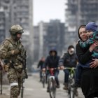 Mariúpol.  Varios civiles caminan, mientras militares ucranianos resguardan una avenida en esta ciudad puerto.