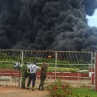 Varios hombres observan una columna de humo generada por el incendio en un depósito de combustible hoy, en Matanzas.
