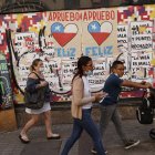 Varias personas caminan frente a una pared con información relacionada al plebiscito constitucional en Santiago (Chile).