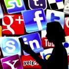 Una mujer revisa su teléfono frente a una pantalla que muestra los íconos de las redes sociales más populares.