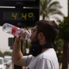 Un joven bebe agua junto a un termómetro de calle que marca 44º, en una fotografía de archivo.