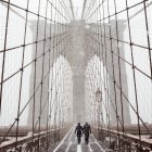 Fotografía de archivo en la que se registró a un par de transeúntes al cruzar el puente de Brooklyn, bajo una tormenta de viento y nieve, en Nueva York (NY, EE.UU.).