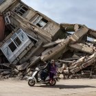 Varias personas pasan con una moto frente a un edificio destruido por los terremotos de Turquía.