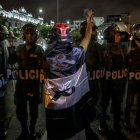 Un manifestante envuelto en una bandera peruana con color negro en lugar del rojo, se para frente a policías, en una fotografía de archivo.
