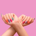 Female hands: one with long colorful nail design and other with short nail design. Glitter nail polish manicure: purple, green, pink, and orange. Female model hands with perfect colorful manicure on p