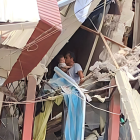 Escenario. Es un hombre, aferradose a lo que queda de una pared y con los pies sobre una casa a punto de derrumbarse, pero quien se muestra feliz de que la vida que carga en sus brazos esté intacta.