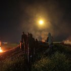 Los palestinos observan un cohete disparado hacia Israel mientras se reúnen entre neumáticos en llamas cerca de la frontera con Israel en Gaza.