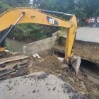 Una retroexcavadora prepara el terreno para levantar un paso vehicular temporal.