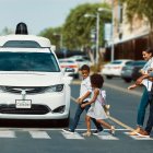 Algunas personas utilizan un paso cebra mientras una unidad sin conductor de Waymo, espera el cambio de luz.