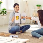 Professional children"s psychologist talking to little kid about emotions. Girl chooses happy smiley emoticon from two EQ cards that female therapist shows her during interview appointment meeting