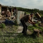 Mykola (R), de 58 años, corta leña mientras su madre Nina, de 92, se sienta en su patio entre los restos de su casa en el pueblo de Bohorodychne, región de Donetsk, Ucrania