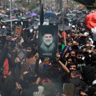 Los musulmanes chiítas iraquíes cantan eslóganes y llevan una imagen de Muqtada al-Sadr y copias del Corán mientras el humo está en el aire durante una reunión después de las oraciones del viernes en la ciudad de Sadr en Bagdad, Irak.