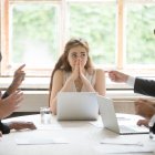 Perplexed young woman looking at coworkers pointing fingers at her. Disgruntled multiethnic team scolding female colleague who made bad work-related mistake. Stressed upset business lady in trouble.