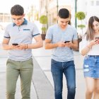 Group of five young boys ands girls walking outdoors in city with their smart phones