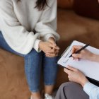 Unrecognizable Psychologist Talking With Female Client Taking Notes During Psychotherapy Session Sitting In Office. Selective Focus, Cropped
