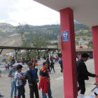 Alausí. Varias personas hacen fila en un recinto electoral. Al fondo, se observa la zona cero del derrumbe.