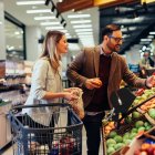 Young adult couple choosing some fresh fruits in grocery store, with shopping trolley beside them