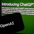 Vista de la página de ChatGPT detrás de un teléfono móvil en el que se ve el logo de la empresa OpenAI