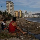 Personas permanecen sentadas junto a los escombros causados por el huracán Otis hoy, en el balneario de Acapulco, en el estado de Guerrero (México)