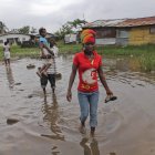 Un grupo de vecinos, con los pantalones remangados y el calzado en la mano, cruzan una zona encharcada.